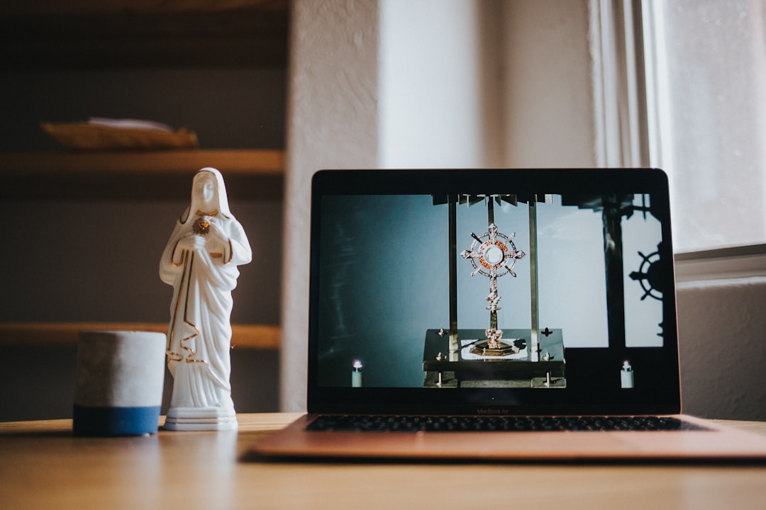 A laptop displaying a religious symbol next to a statue of a saint on a wooden table